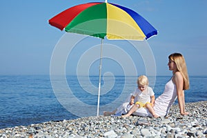 Mother with child under umbrella on pebble beach