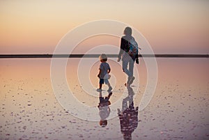 Mother and child walking on a salt and brine of a pink lake, colored by microalgae Dunaliella salina