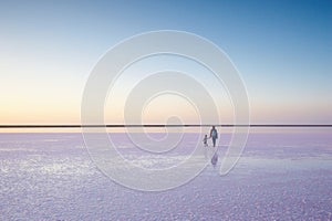 Mother and child walking on a salt and brine of a pink lake, colored by microalgae Dunaliella salina