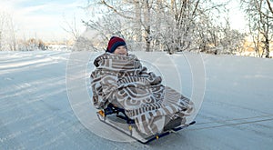 Mother with a child walks on a frosty winter morning on a Sunny day. Baby wrapped in a blanket rides on a sled