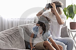 Mother and child wearing virtual reality headset vr glasses in living room at home having fun