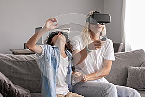 Mother and child wearing virtual reality headset vr glasses in living room at home having fun