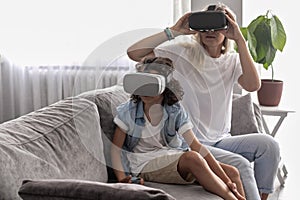 Mother and child wearing virtual reality headset vr glasses in living room at home having fun