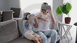 Mother and child wearing virtual reality headset vr glasses in living room at home having fun