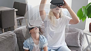 Mother and child wearing virtual reality headset vr glasses in living room at home having fun