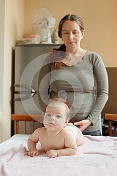 Mother and child on a white bed. Baby girl in diaper. Mom playing with her baby