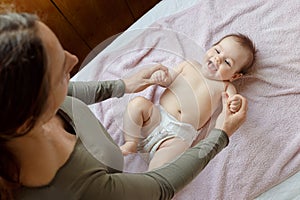 Mother and child on a white bed. Baby girl in diaper. Mom playing with her baby