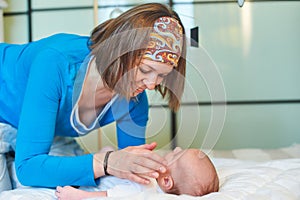 Mother and child on a white bed. Mom and baby boy in diaper playing in sunny bedroom. Mom makes gymnastics for her newborn baby.