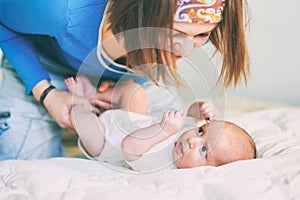 Mother and child on a white bed. Mom and baby boy in diaper playing in sunny bedroom. Mom makes gymnastics for her newborn baby.