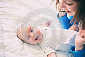 Mother and child on a white bed. Mom and baby boy in diaper playing in sunny bedroom. Mom makes gymnastics for her newborn baby.