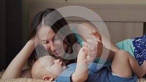 Mother and child on a white bed. Mom and baby boy in diaper playing in sunny bedroom. Parent and little kid relaxing at