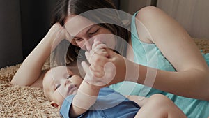 Mother and child on a white bed. Mom and baby boy in diaper playing in sunny bedroom. Parent and little kid relaxing at