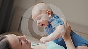 Mother and child on a white bed. Mom and baby boy in diaper playing in sunny bedroom. Parent and little kid relaxing at