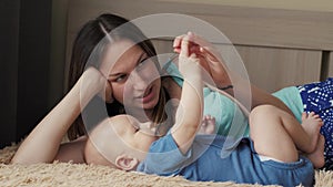 Mother and child on a white bed. Mom and baby boy in diaper playing in sunny bedroom. Parent and little kid relaxing at