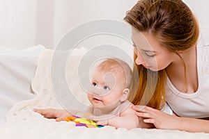 Mother and child on a white bed. Mom and baby boy in diaper playing in sunny bedroom.