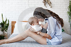 Charming happy little baby boy having fun with mom brunette woman on bed in the bright bedroom