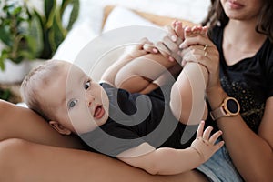 Charming happy little baby boy having fun with mom brunette woman on bed in the bright bedroom