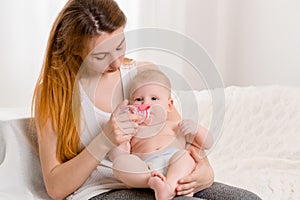 Mother and child on a white bed. Mom and baby girl in diaper playing in sunny bedroom.