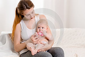 Mother and child on a white bed. Mom and baby girl in diaper playing in sunny bedroom.
