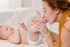 Mother and child on a white bed. Mom and baby girl in diaper playing in sunny bedroom.