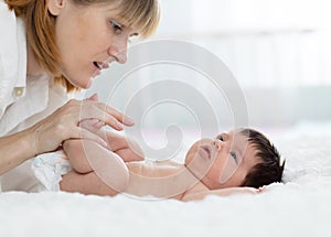 Mother and child on white bed. Parent and little kid relaxing at home. Mom doing massage baby.