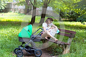 Mother and child, young mom is parenting her little toddler, woman breastfeeding and holding her baby, sitting on a park bench