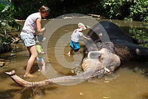 Mother with children caressing Asian elephant in captivity, chained, abused for attracting tourists photo