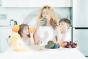 Mother and children daughter and son drinking green smoothie in the kitchen with fruits and vegetables. Happy Family