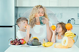 Mother and children daughter and son drinking green smoothie in the kitchen with fruits and vegetables. Happy Family