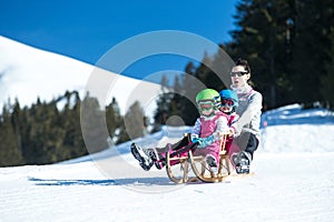 Mother and children having fun on sledge with panoramatic view of Alps mountains. Active mom and toddler kid with safety helmet.