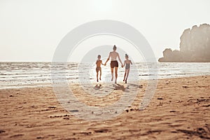 Mother and children holding hands and skipping along a beach