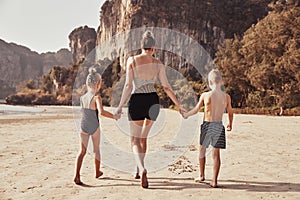 Mother and children holding hands while walking on a beach