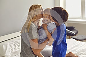 Mother and children hug and kiss on the bed in the room. Mothers Day. Mom and sons cuddle up.