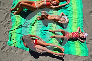 Mother and children lying on coverlet on beach photo