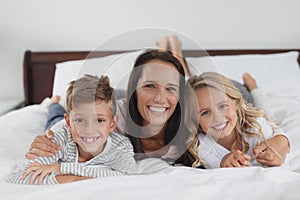 Mother and children lying together on bed in bedroom at home