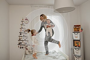 Mother and children in pajamas jumping on the bed in the morning