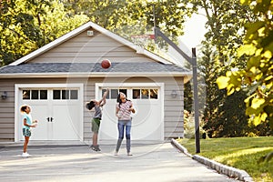 Mother And Children Playing Basketball On Driveway At Home