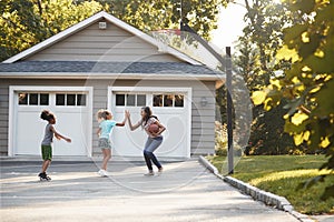 Mother And Children Playing Basketball On Driveway At Home