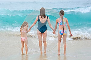 Mother and children playing on the ocean beach. Family enjoying the ocean. Mother holds girls's hands and they all