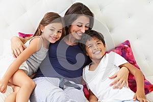 Mother And Children Relaxing In Bed Wearing Pajamas