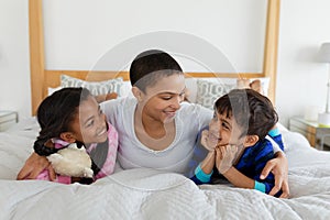 Mother and children relaxing together on bed in bedroom