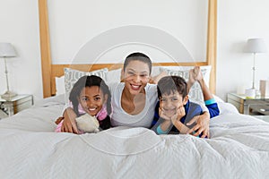 Mother and children relaxing together on bed in bedroom at home