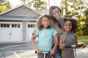 Mother With Children Riding Scooters On Driveway At Home