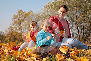 Mother with children sit on fallen maple leaves