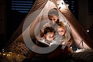 Mother with children sitting indoors in bedroom, reading a book.