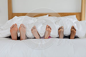 Mother and children sleeping barefoot in bed in bedroom at home