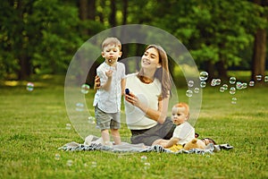 Mother with children with soap bubbles in summer park.