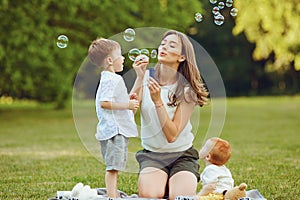 Mother with children with soap bubbles in  park.