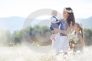 Mother with children in a summer field of blooming daisies