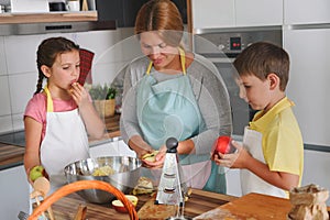 Mother and children together making apple pie in the kitchen at home. Children helping mother